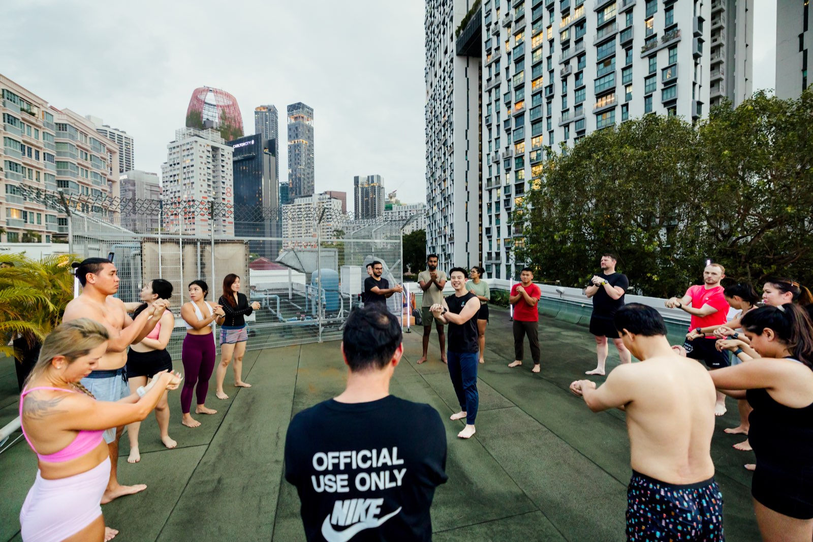 A class standing in a circle on the rooftop deck, hands pressed together in front of them, high-rise towers behind