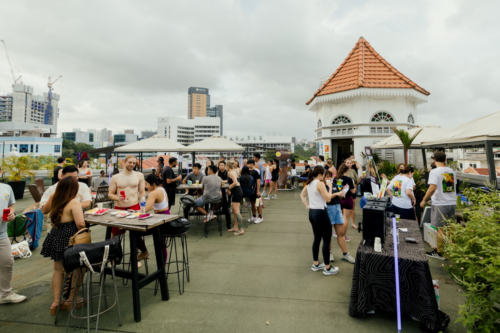 Wide view across the rooftop: high tables, partner stalls, the white turret and the city beyond